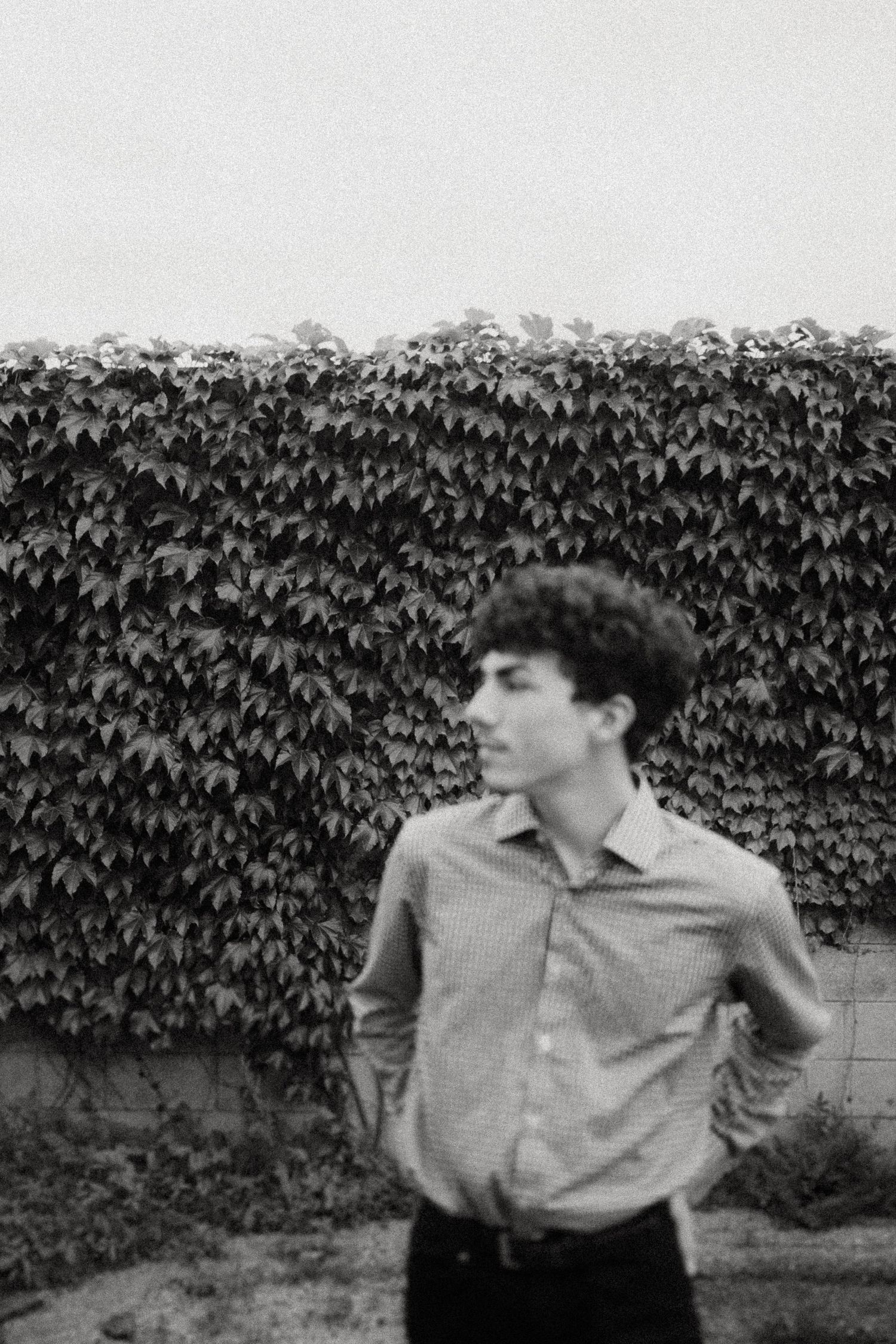A vintage-style black and white portrait against an ivy-covered wall in a moody setting.