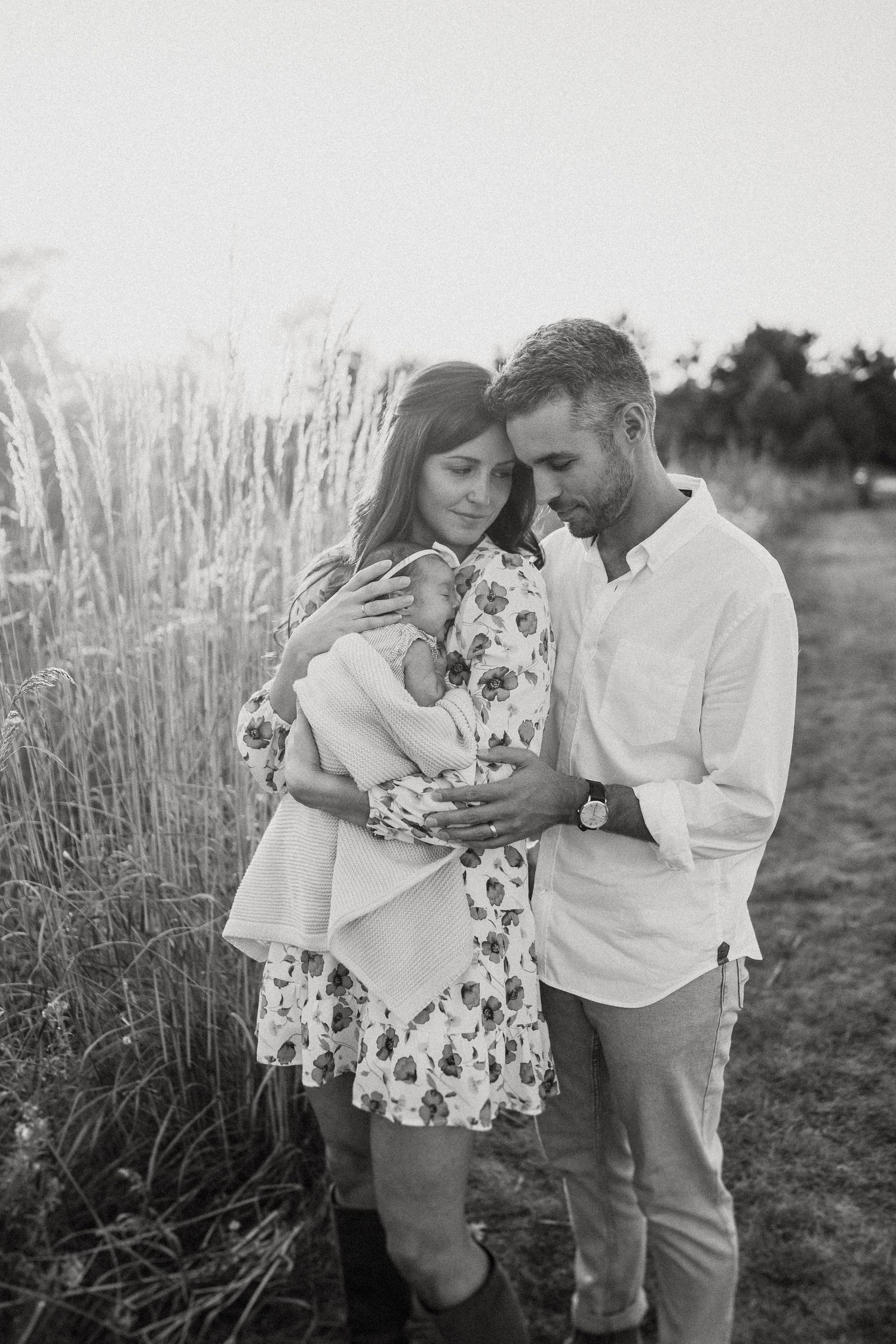 Black and white intimate family portrait with floral dress in outdoor field setting.