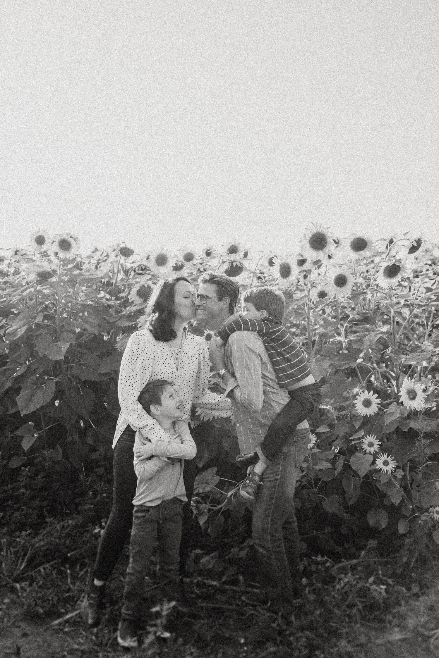 Family embracing in black and white photography with sunflowers as backdrop.