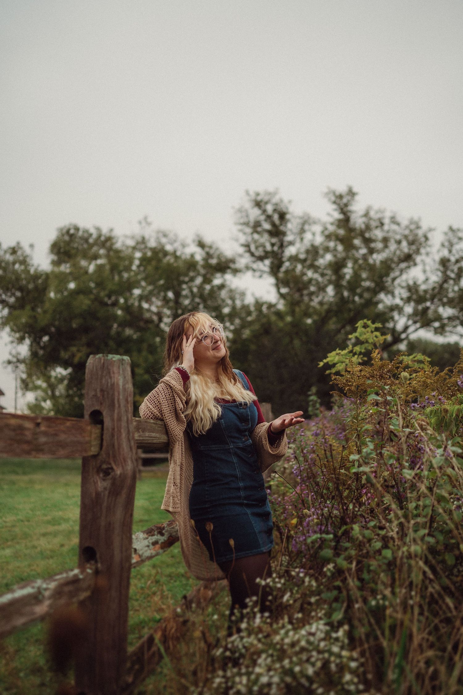 Rustic outdoor portrait by wooden fence post with wild flowering bushes.