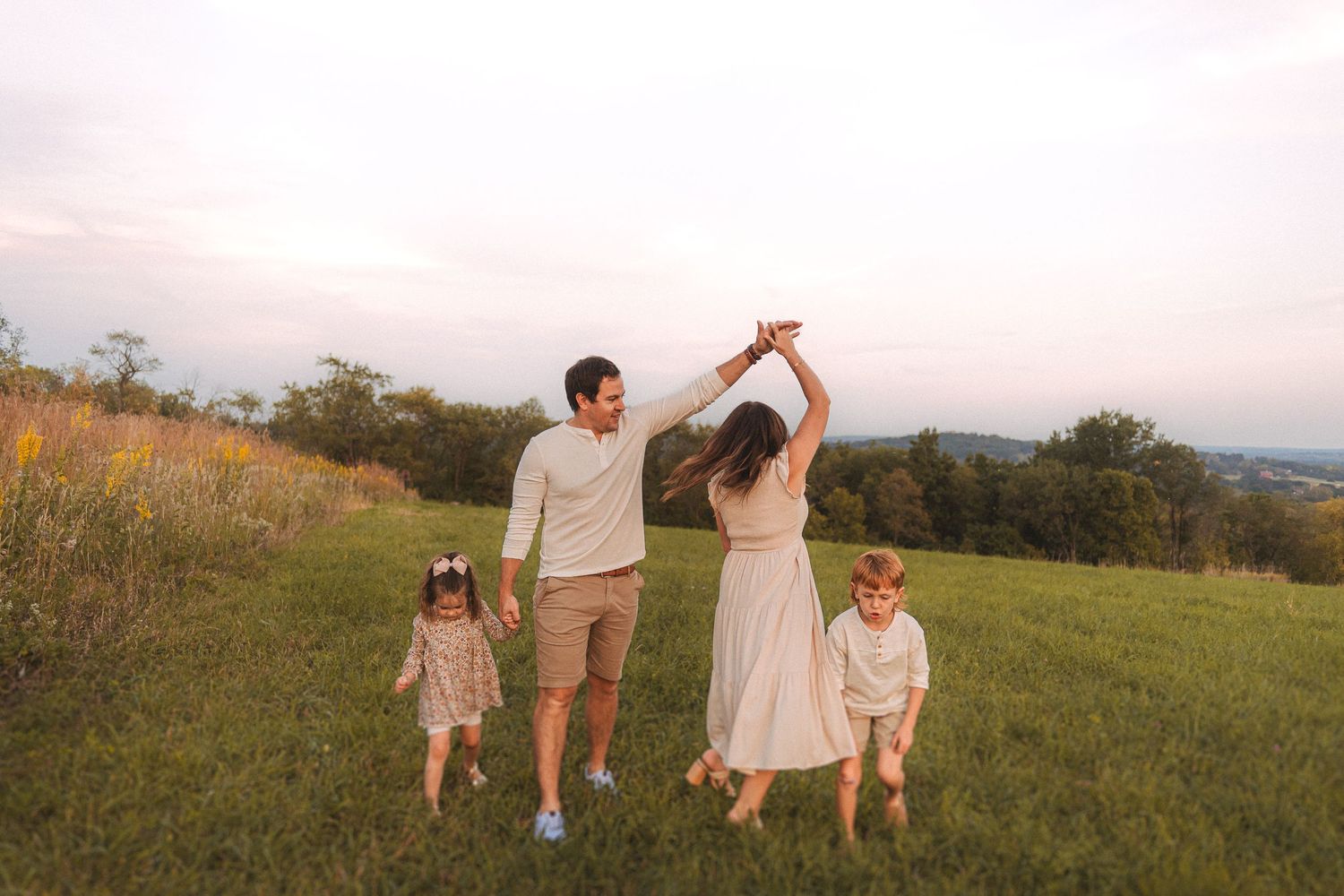 Family dancing and twirling together in a sunlit meadow.