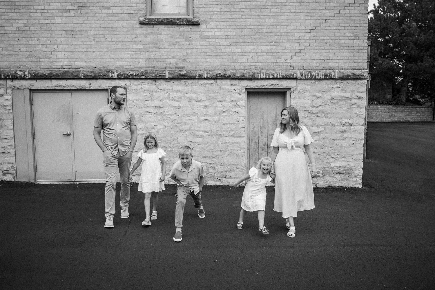 Group in white dresses walking along brick wall of building in black and white photo.