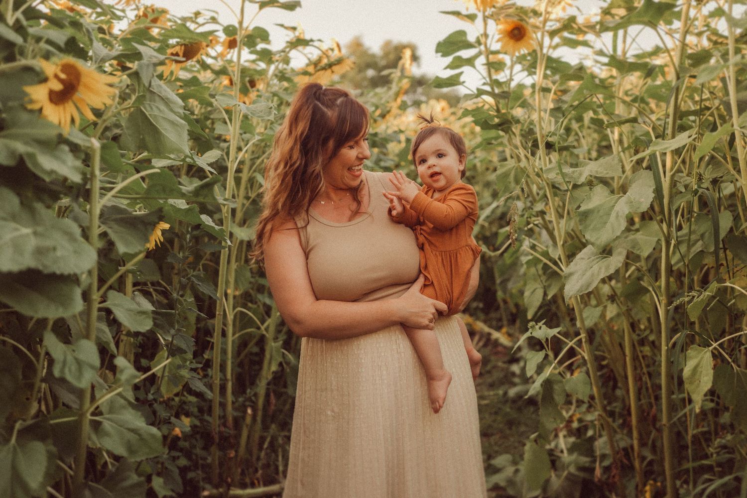 A tender family moment shared in a golden sunflower field at sunset.