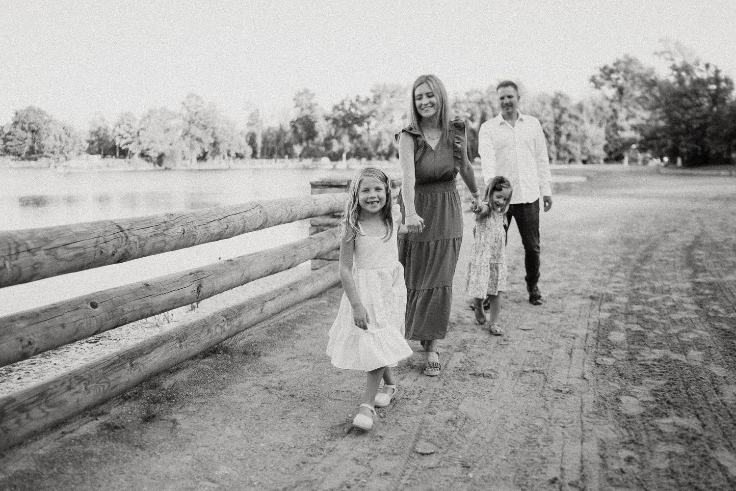 Black and white photo of a family walking together along a rustic fence path.