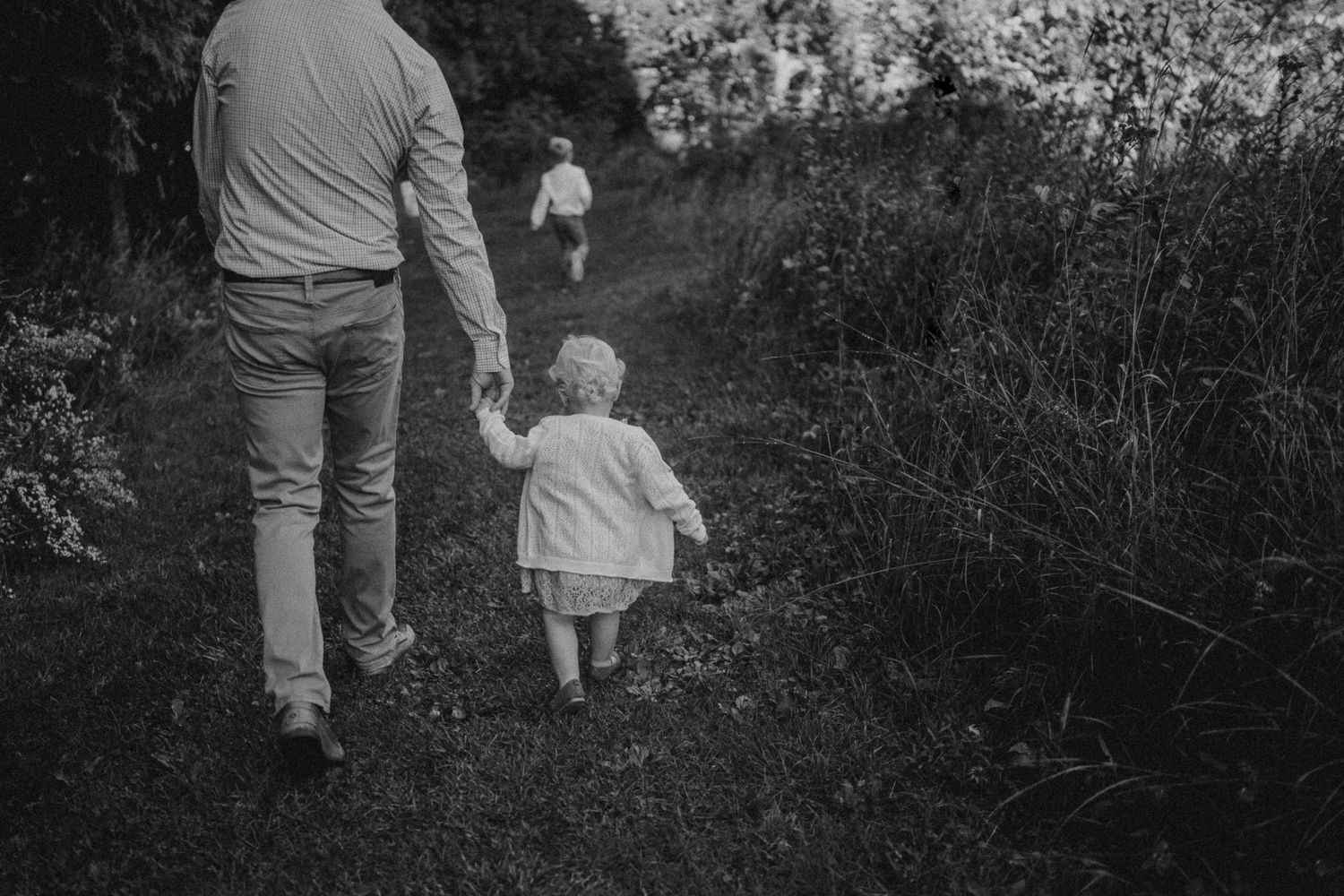 Black and white image of a parent and child walking hand in hand on a nature path.