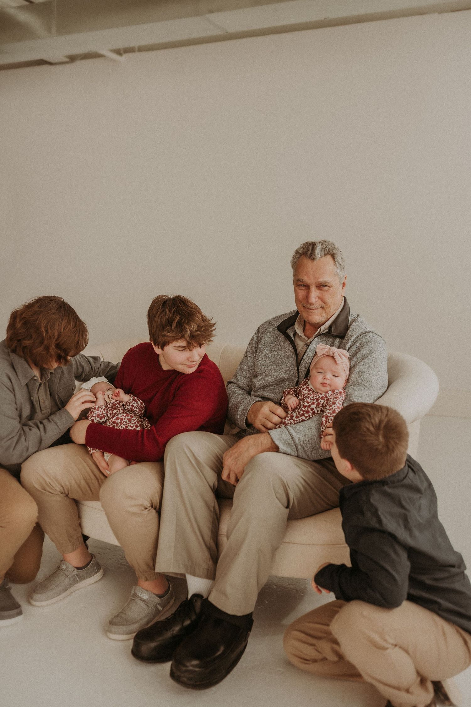 A family group sits together on a cream-colored couch while bonding in a bright studio setting.