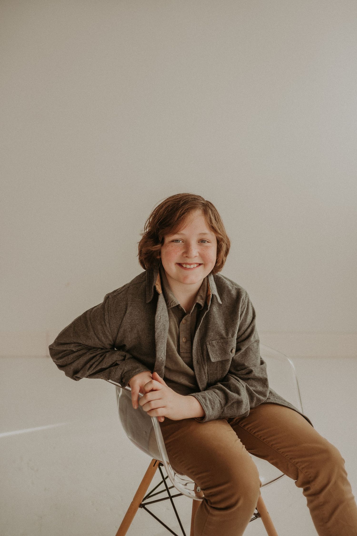 A seated figure in a brown jacket smiles warmly while sitting on a modern white chair.