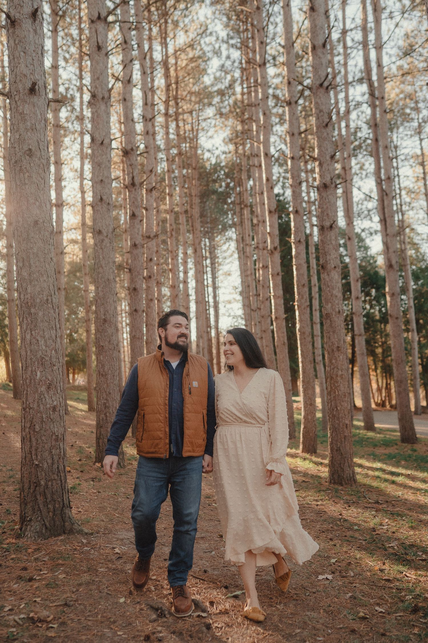 A couple walks together through a sunlit pine forest on an autumn afternoon.