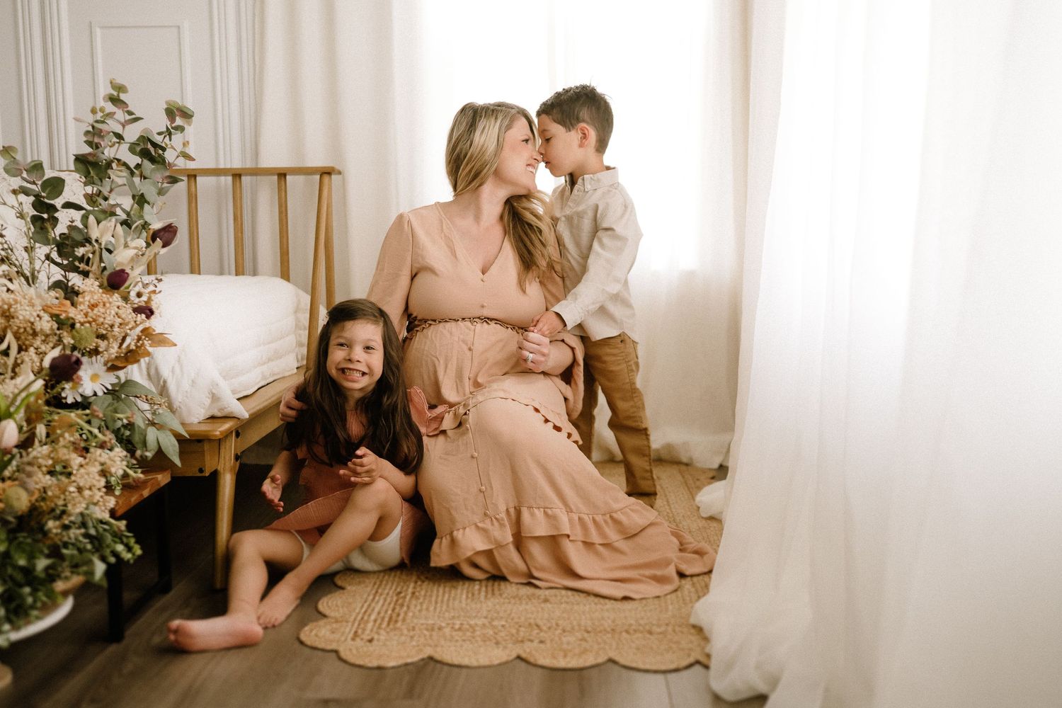 A relaxed family moment captured in soft beige tones with natural light and floral decor beside them.