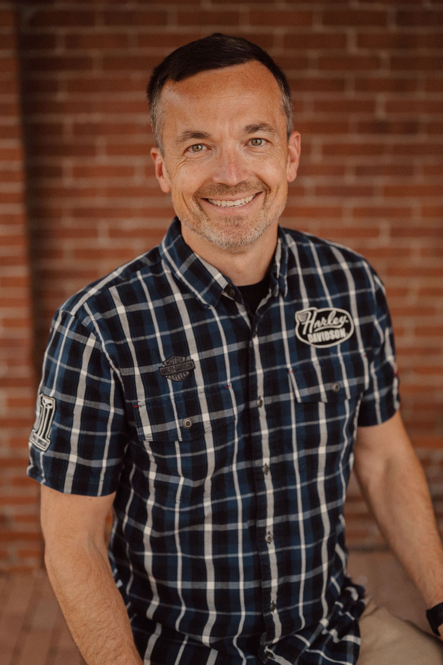 Portrait series against brick wall showing person in plaid shirt with warm lighting.
