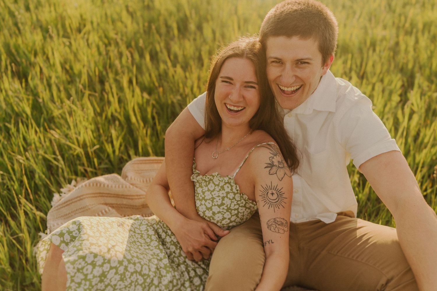 Happy couple sharing a joyful moment while sitting in a sun-drenched wheat field.