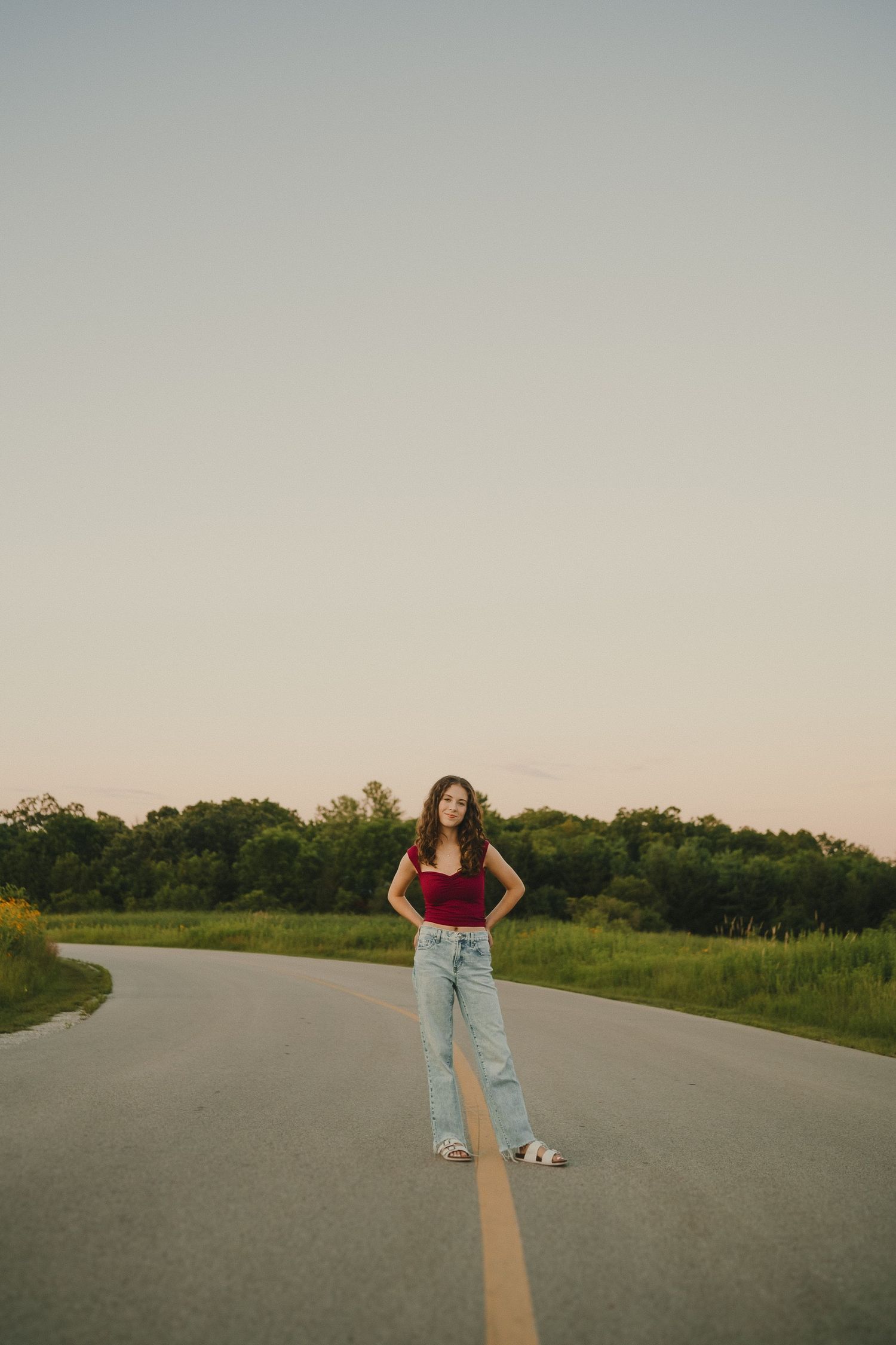 Someone in casual attire stands confidently on a rural road during sunset.
