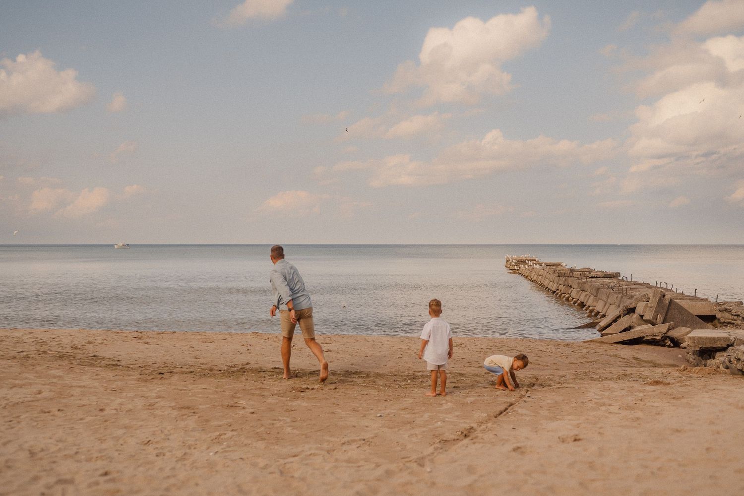 Walking along a rocky beach pier during sunset with calm waters stretching to the horizon.