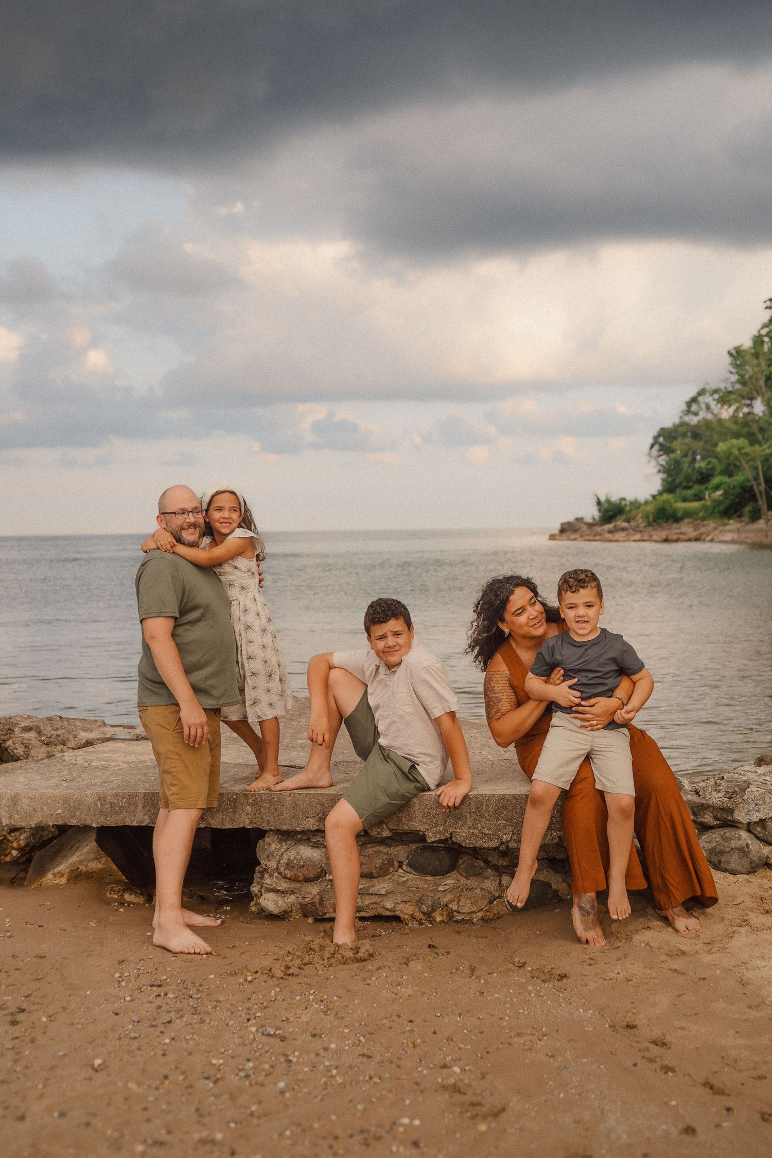 Family members sit casually on large rocks by the ocean shore during golden hour.
