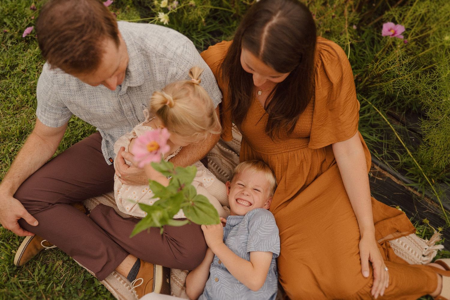 Family members in earth-toned clothing share tender moments outdoors in a golden sunlit natural setting.