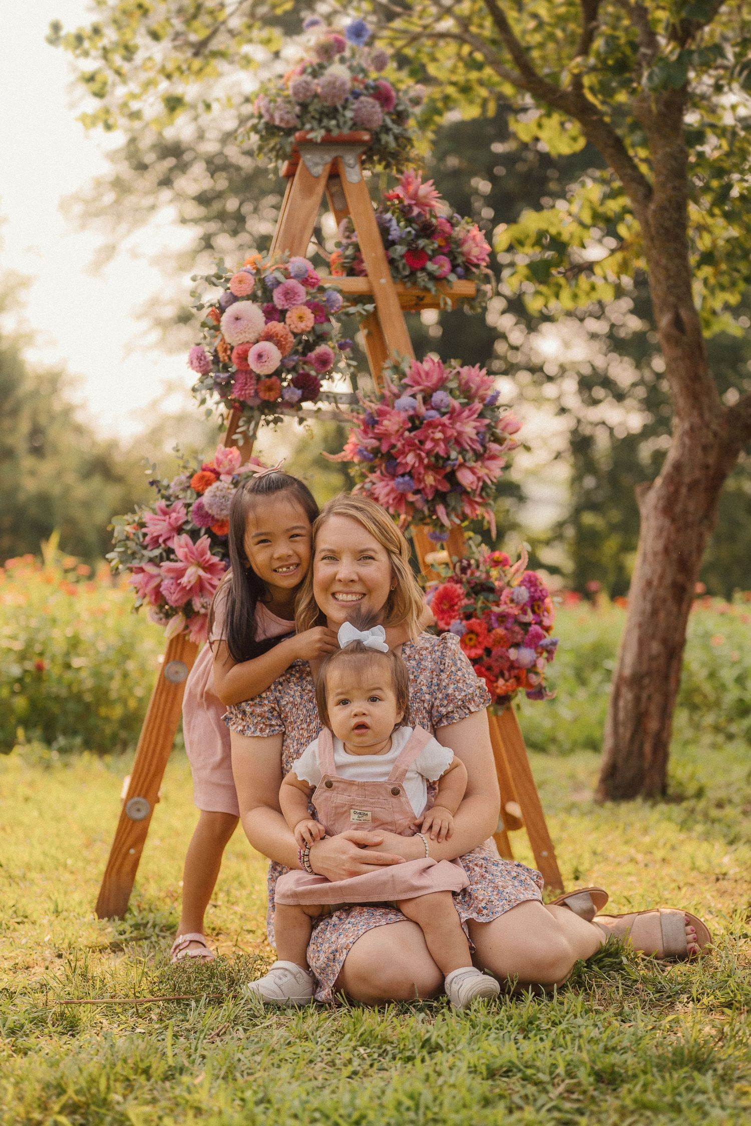 Candid family moment captured under a wooden arch decorated with pink flowers in a summer garden.
