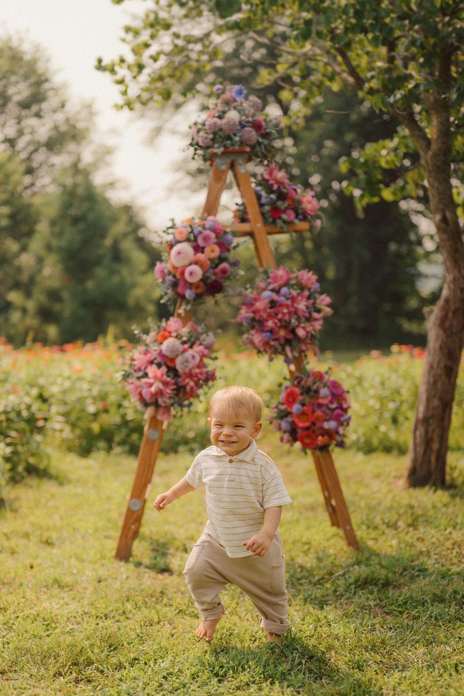 A child plays joyfully in a grassy outdoor garden decorated with wooden stands adorned with pink flowers.