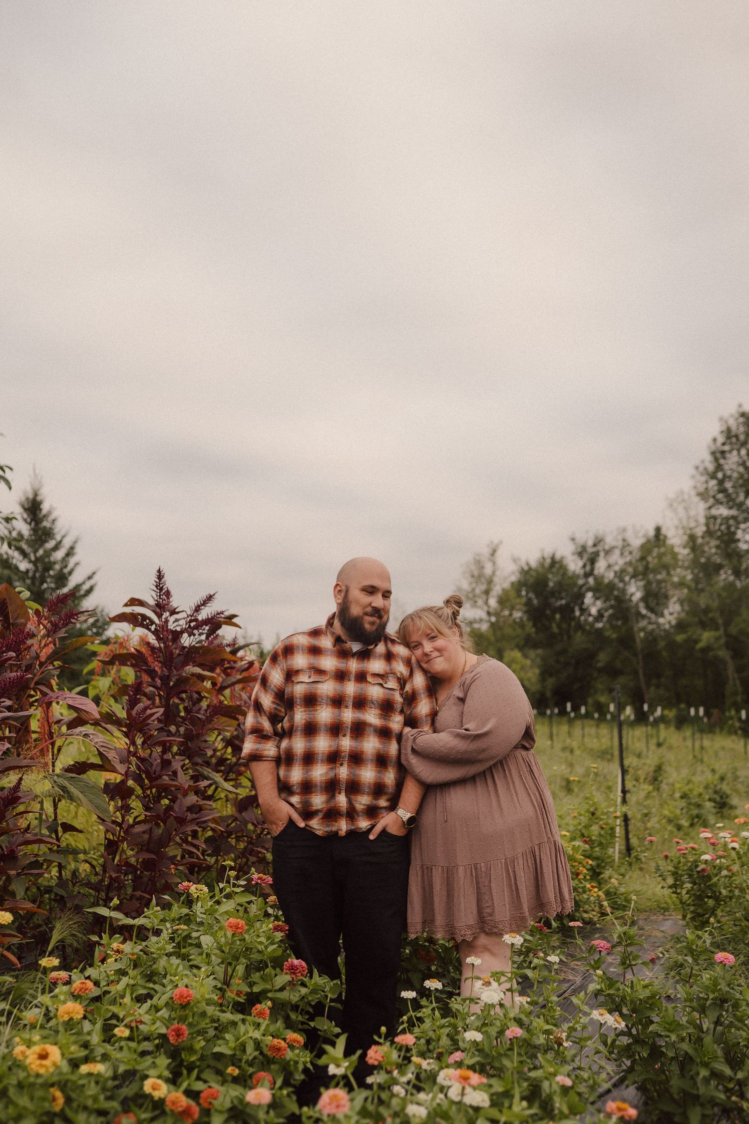 Romantic couple shares tender moments in a garden filled with blooming flowers and lush greenery under cloudy skies.