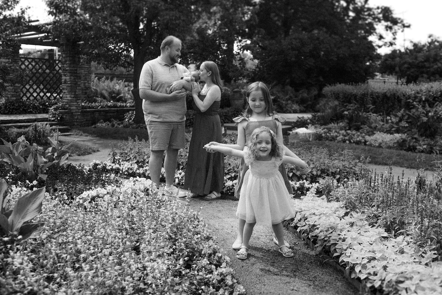 Black and white portrait of a family gathered in a blooming garden with white flowers along a curved pathway.