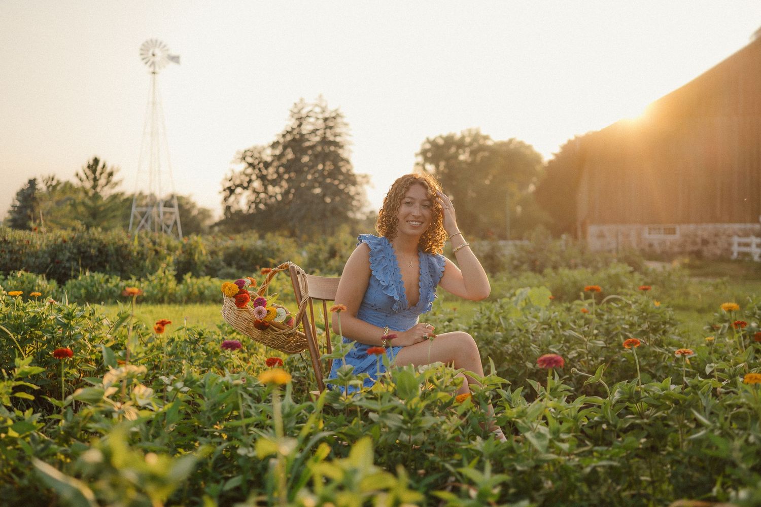 A person in a blue dress sits in a blooming flower garden at sunset while golden light illuminates the scene.