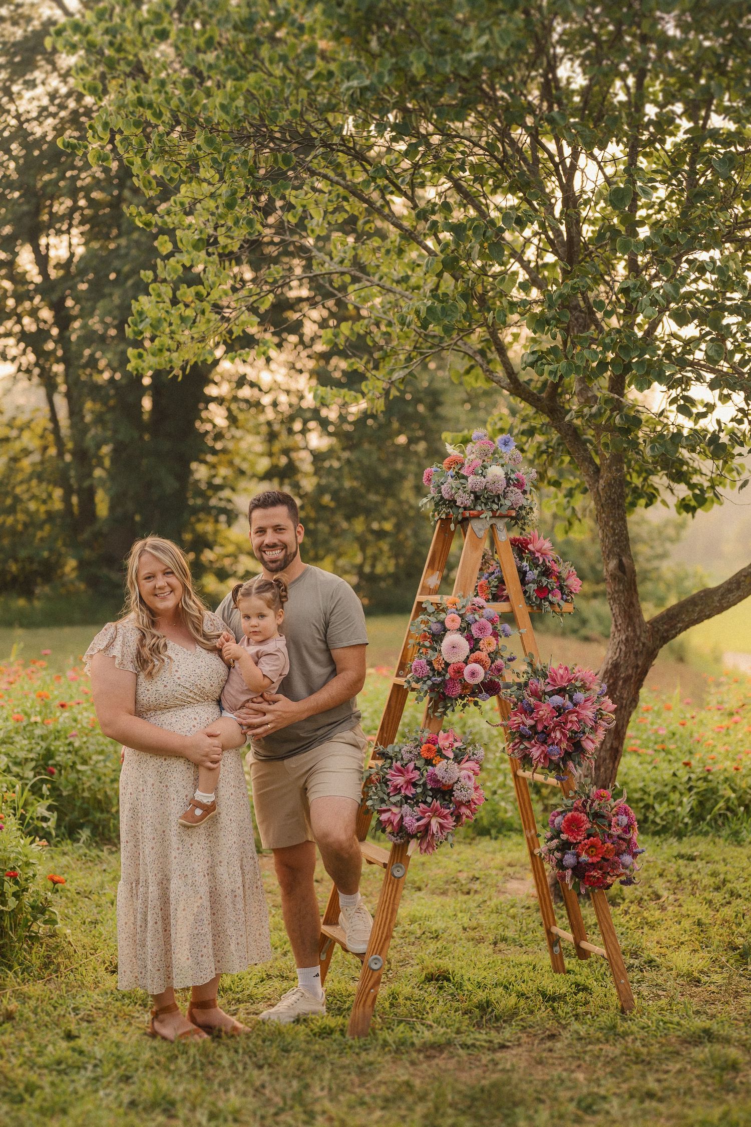 Outdoor family photo session with wood ladder and pink floral arrangements in golden sunlight.