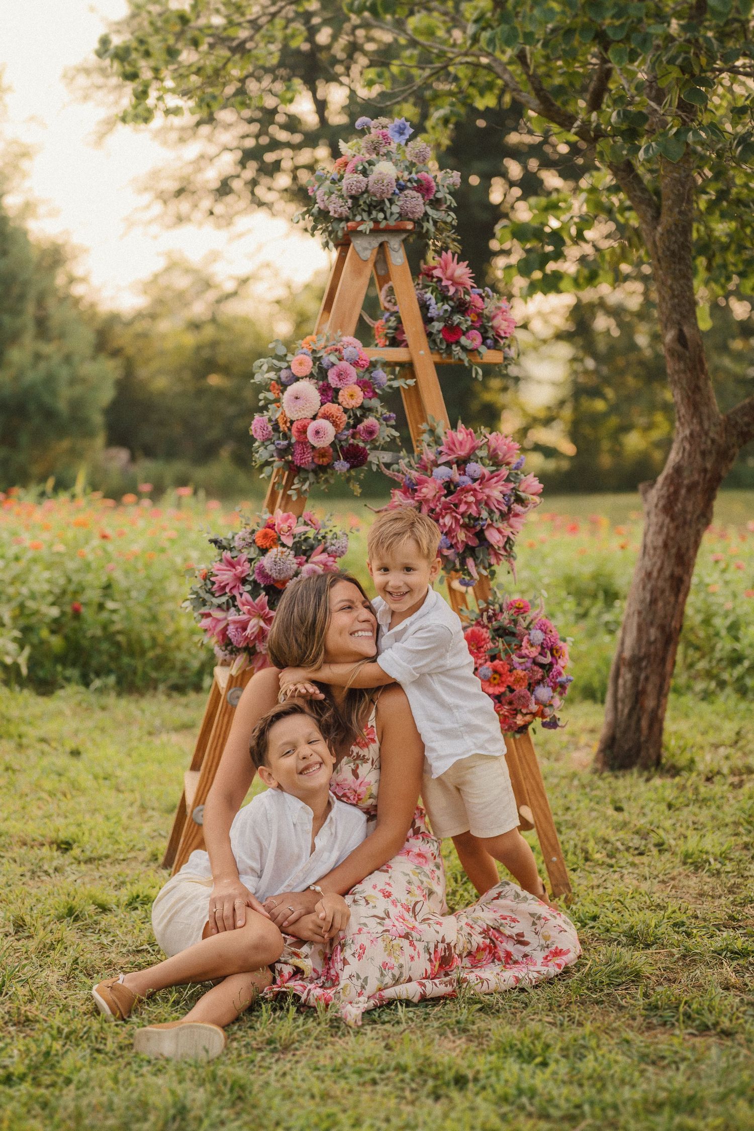 A joyful outdoor family photoshoot with a pink floral ladder display creating a dreamy backdrop in a garden setting.