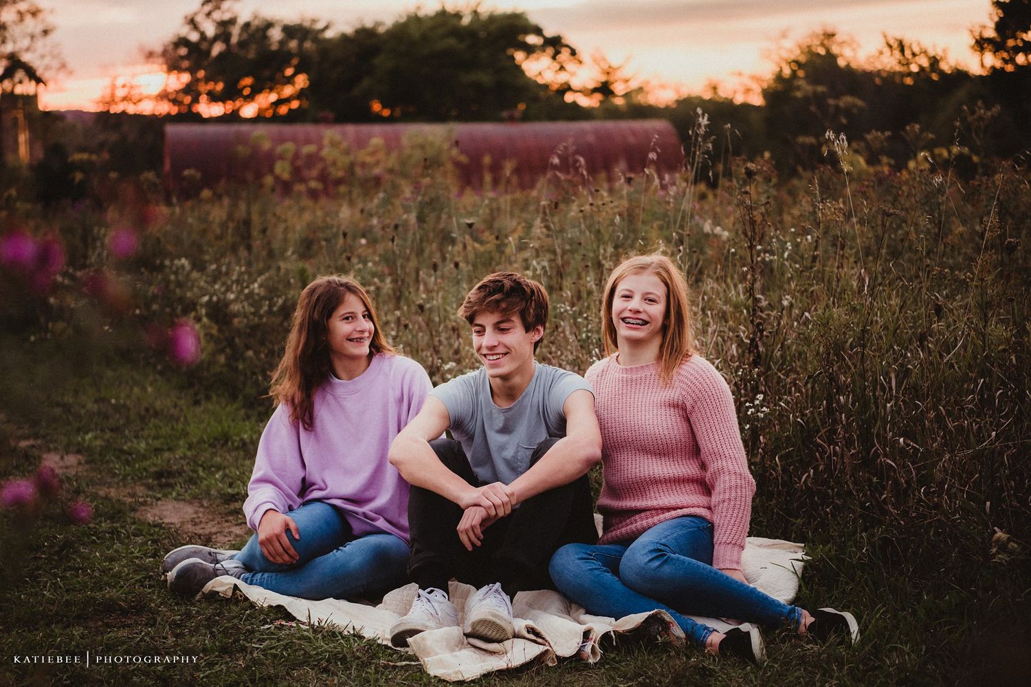 Friends sitting together on a blanket in a field during sunset.