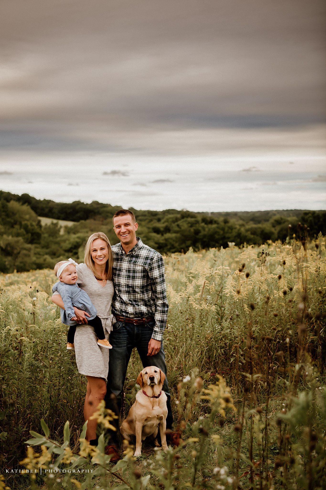 A family portrait in a wildflower field with their golden retriever dog at sunset.