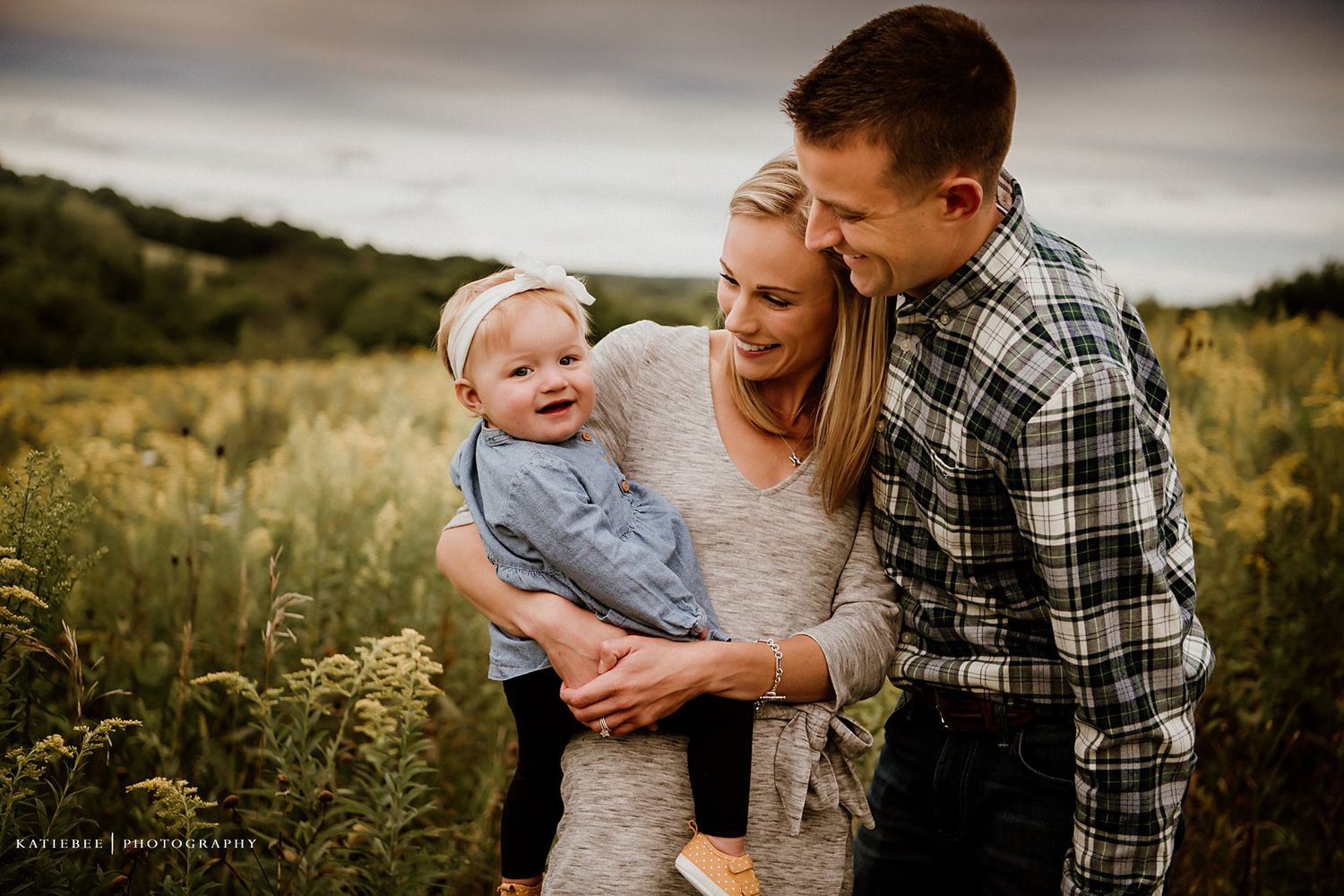 Candid family portrait showing loving embrace in golden field at sunset.