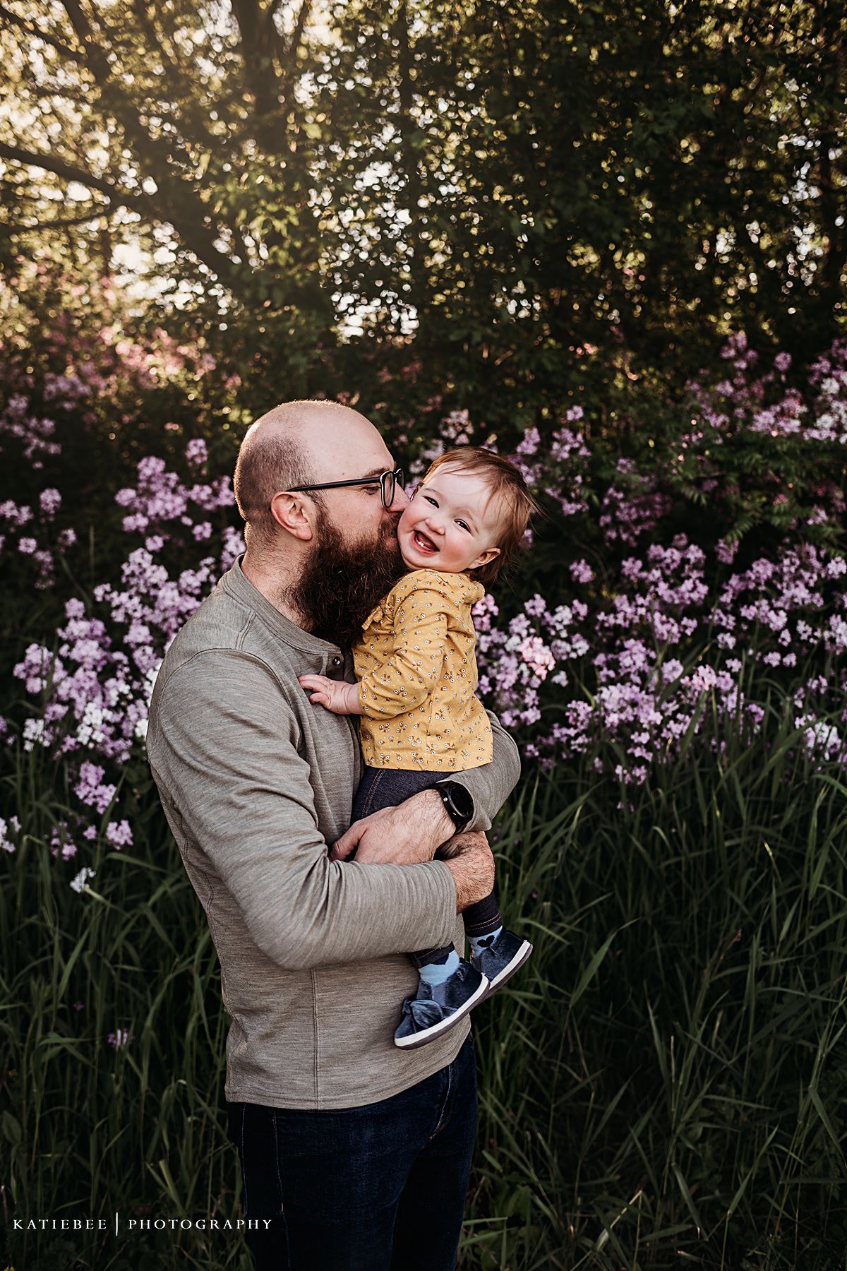 Playful moment between parent and child surrounded by blooming purple flowers in garden setting.