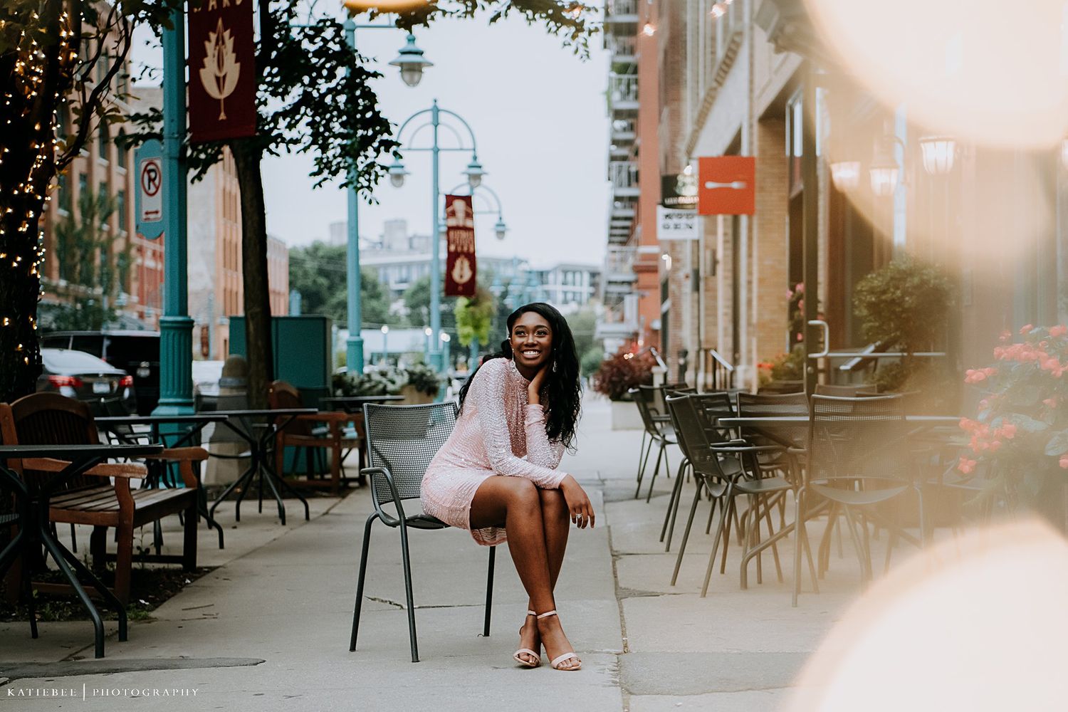 Person in white dress sitting on chair at outdoor cafe setting during sunset.