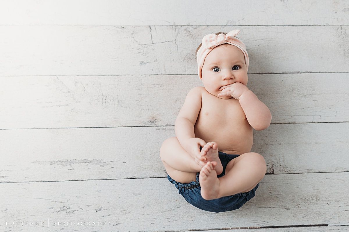 Baby in denim and headband poses against white wooden background during photo session.