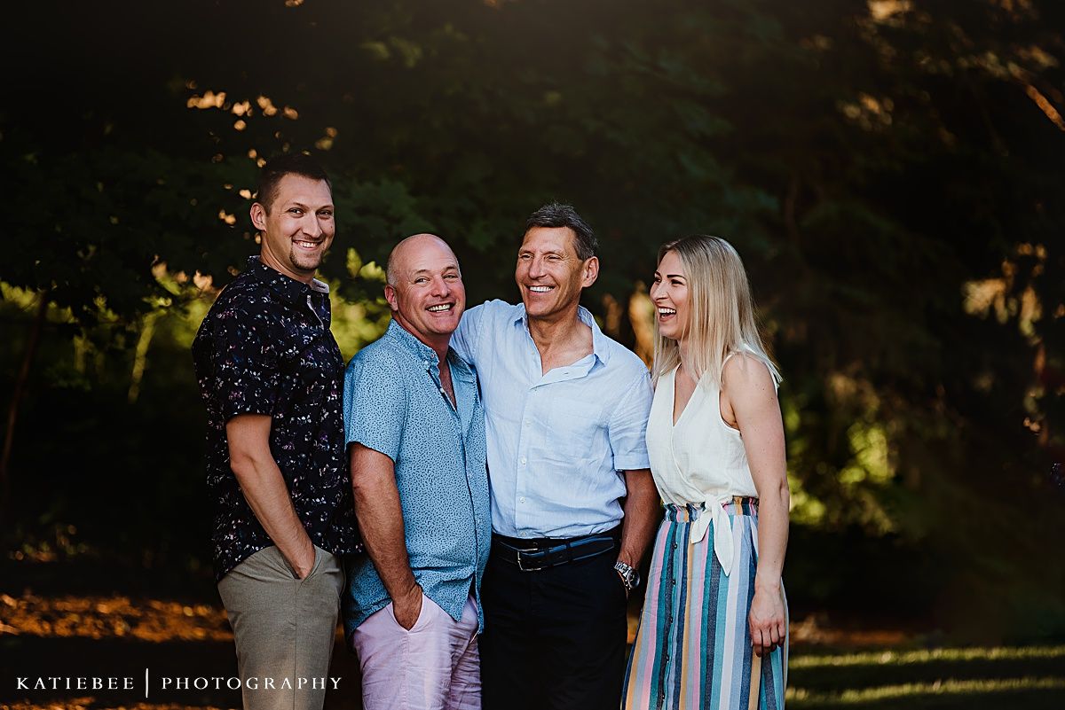 Four people pose together for an outdoor portrait with golden sunlight filtering through trees.