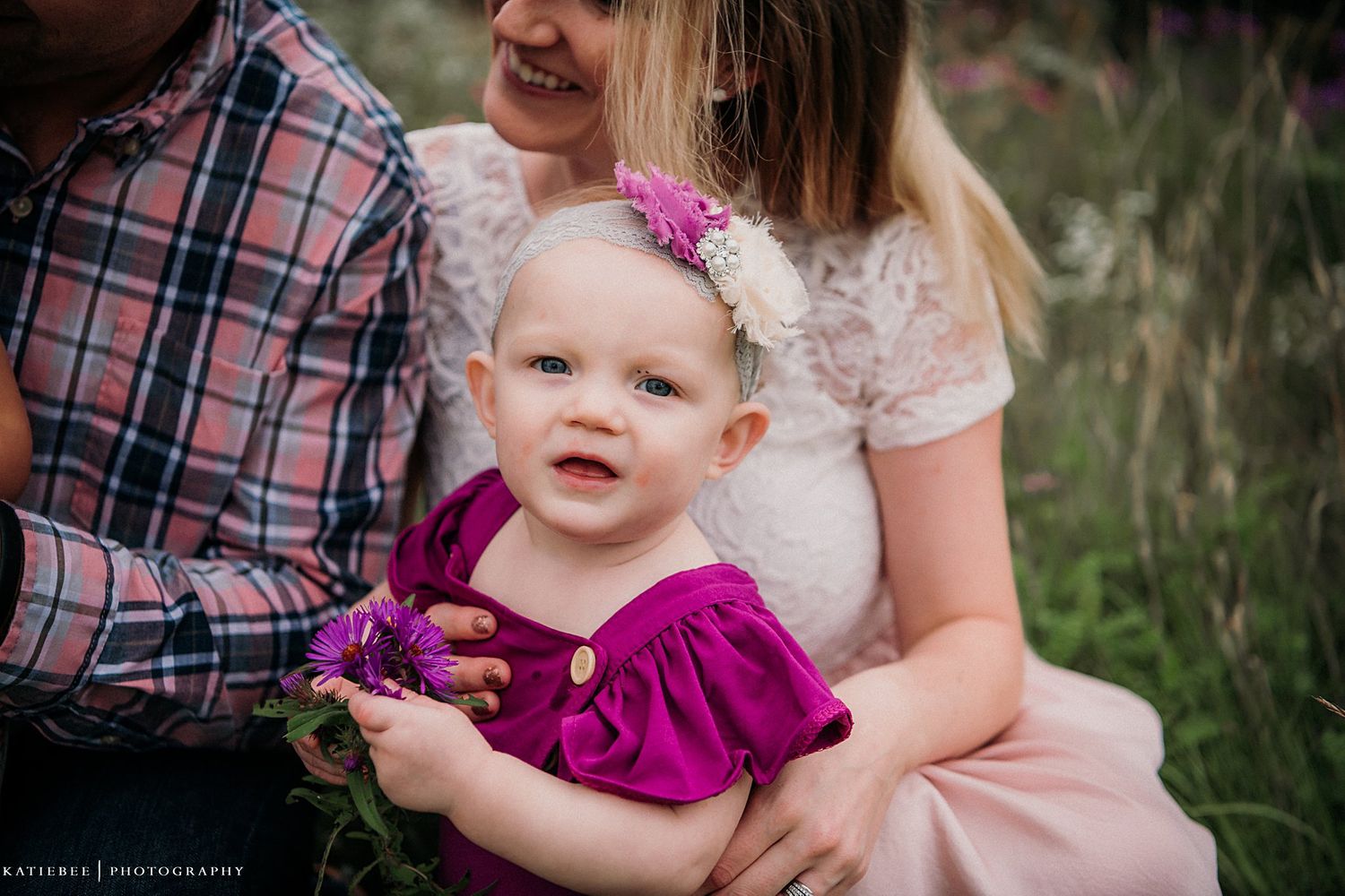 A family portrait captures a tender moment in a field of tall grass.