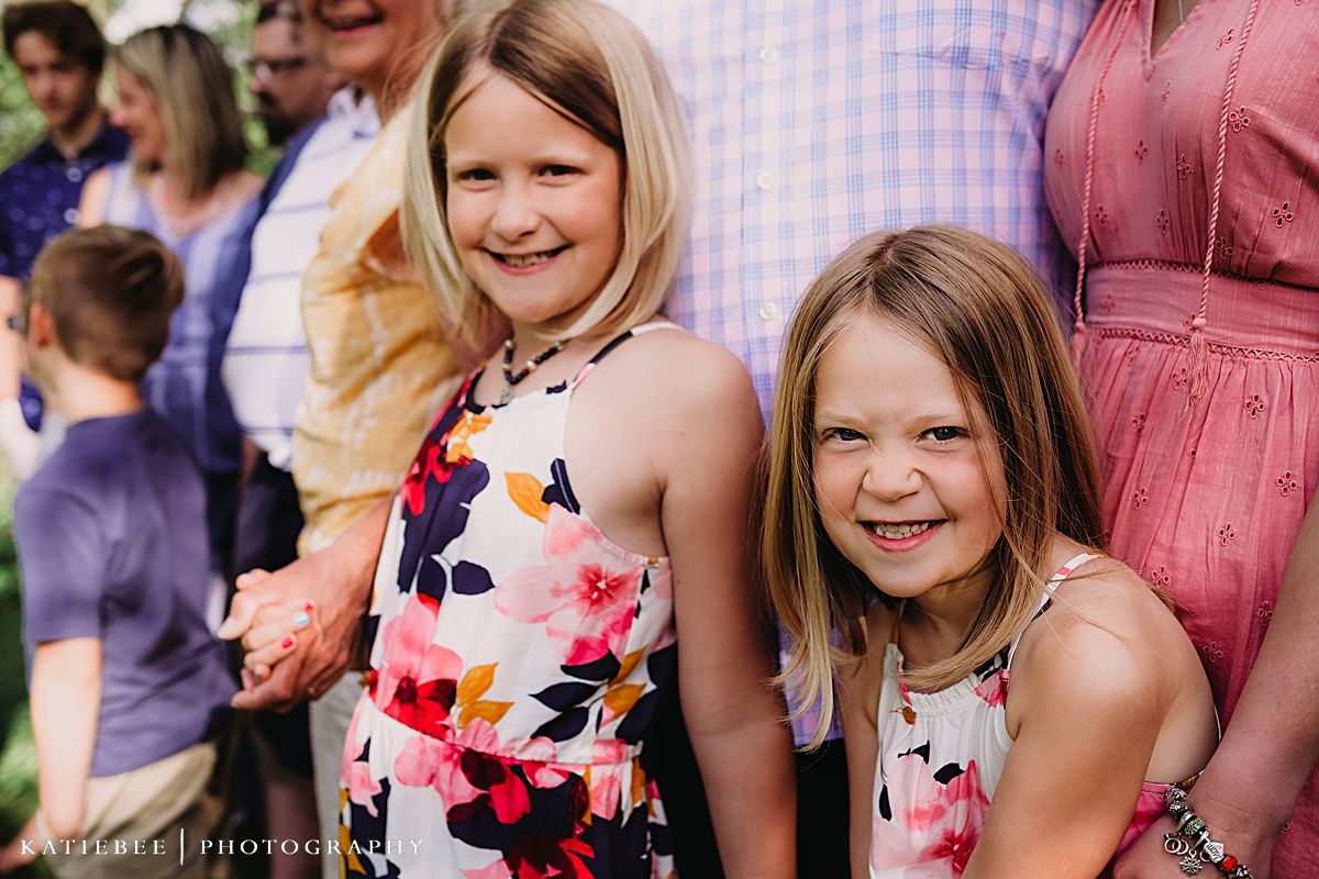 Two children in floral summer dresses pose together at an outdoor gathering.