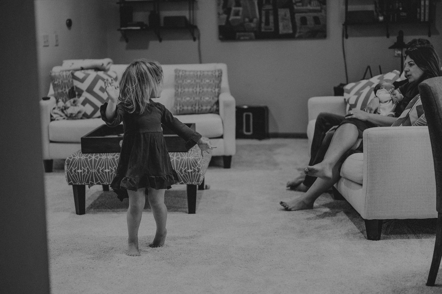 Black and white photo of a toddler dancing in front of a couch while family watches.