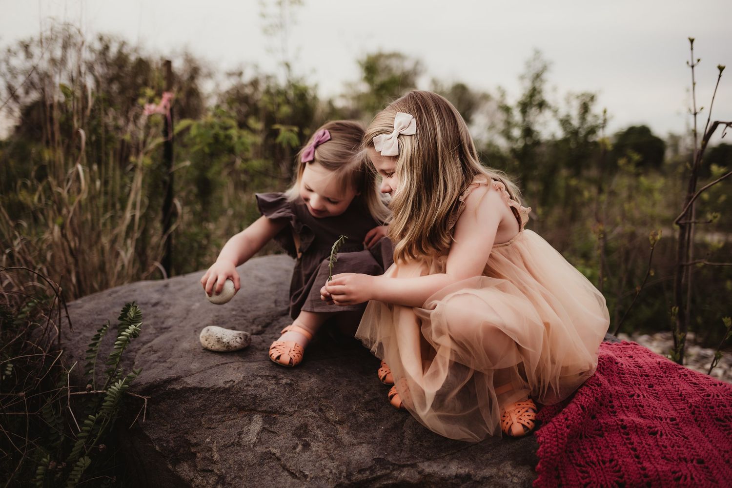 Two figures sit together on a rocky outcrop surrounded by wildflowers at dusk.