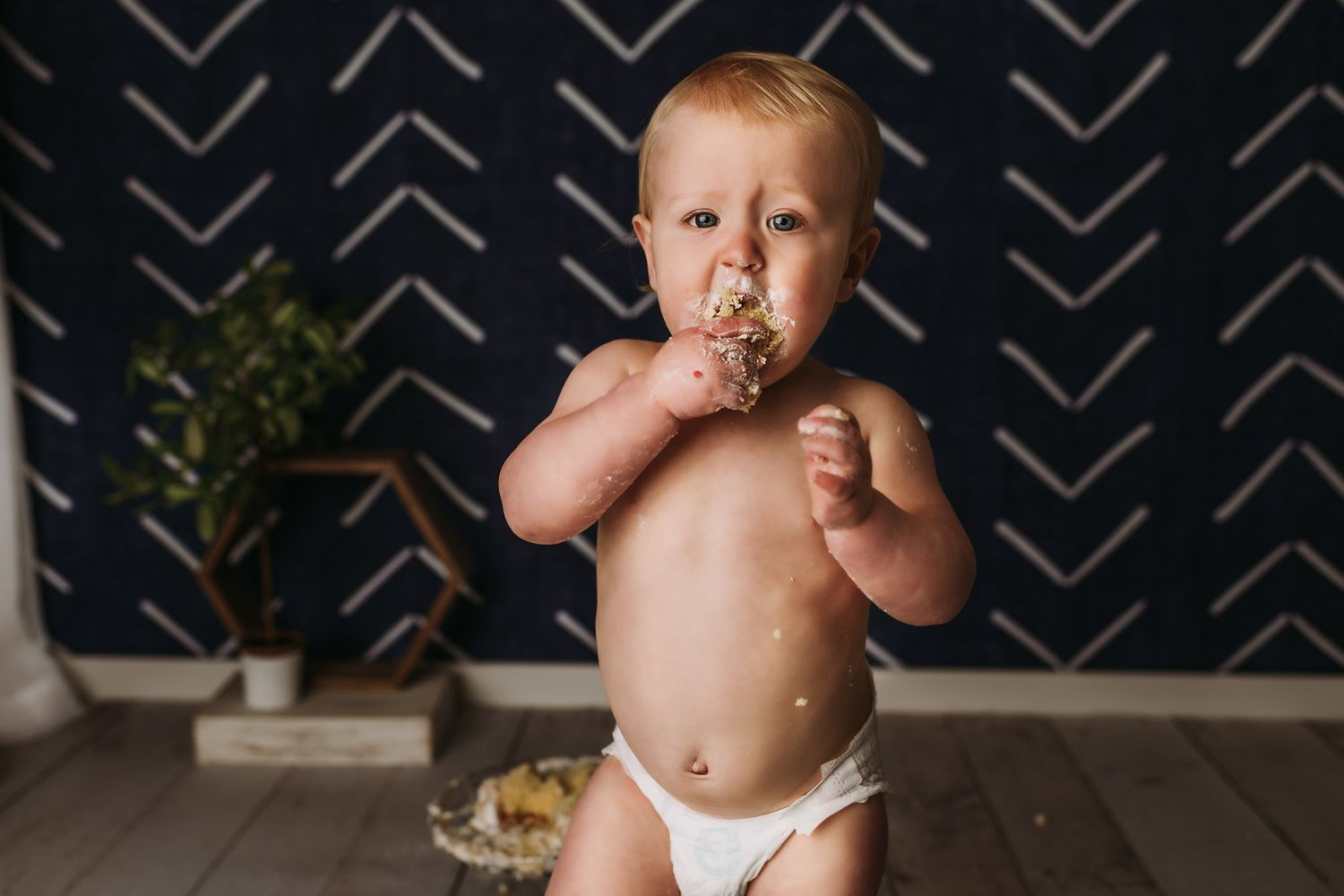Toddler enjoys messy cake against dark geometric wallpaper background.