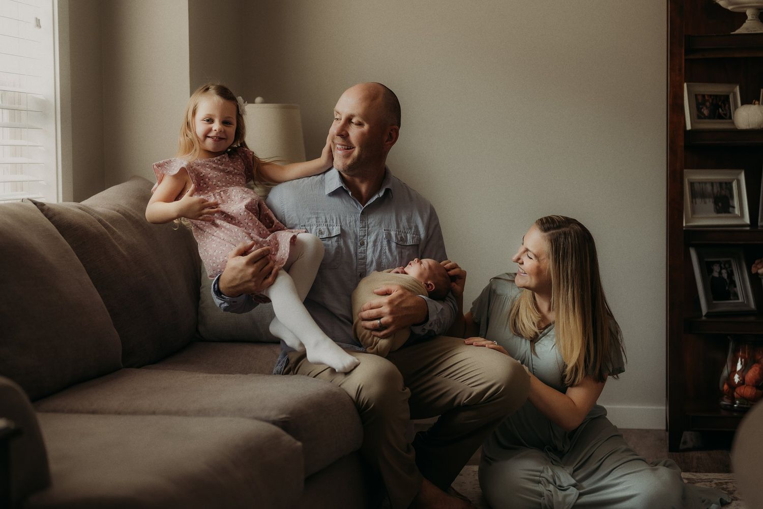 Relaxed family portrait on grey couch with natural window lighting.