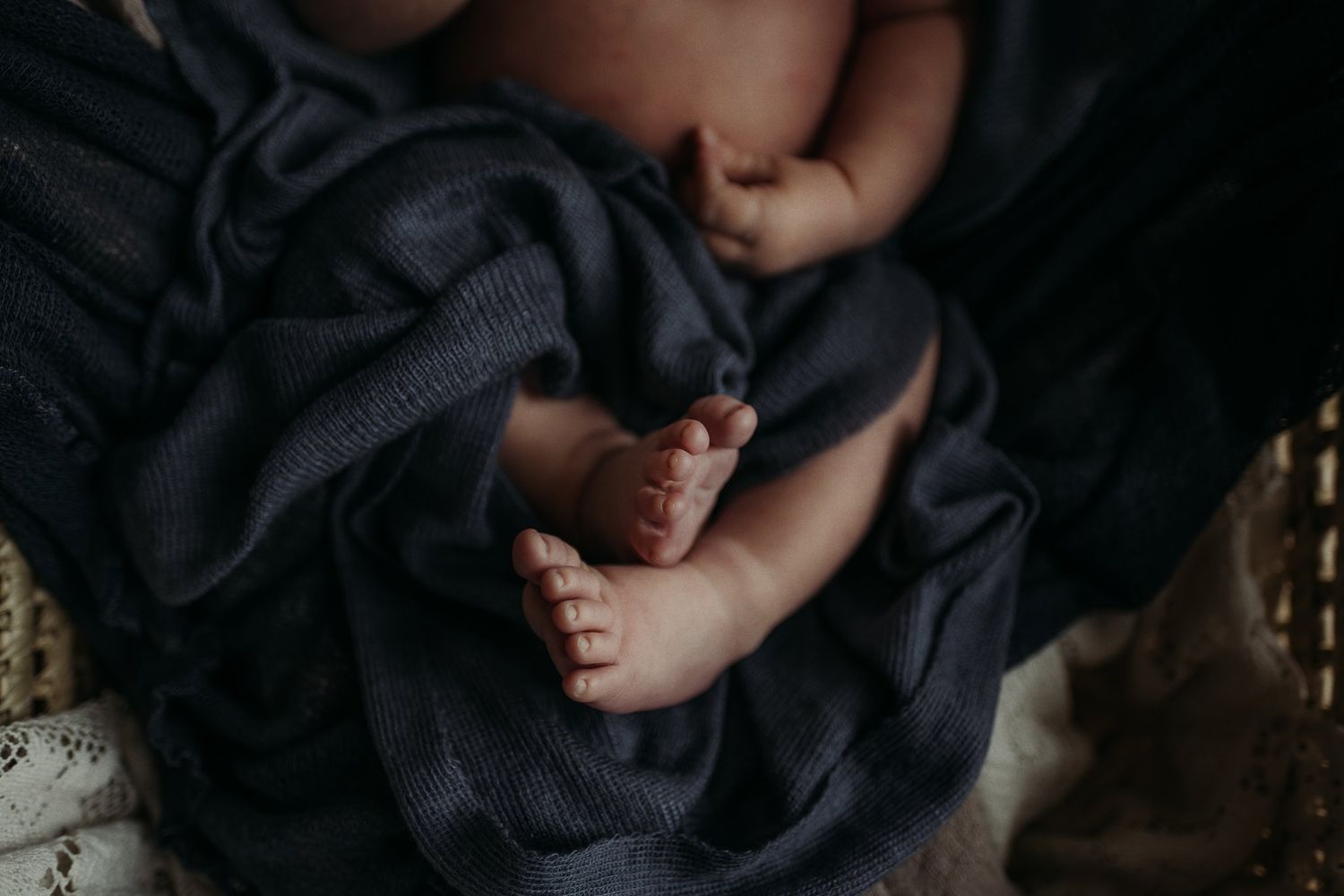 Tiny baby feet and legs against dark navy blue fabric.