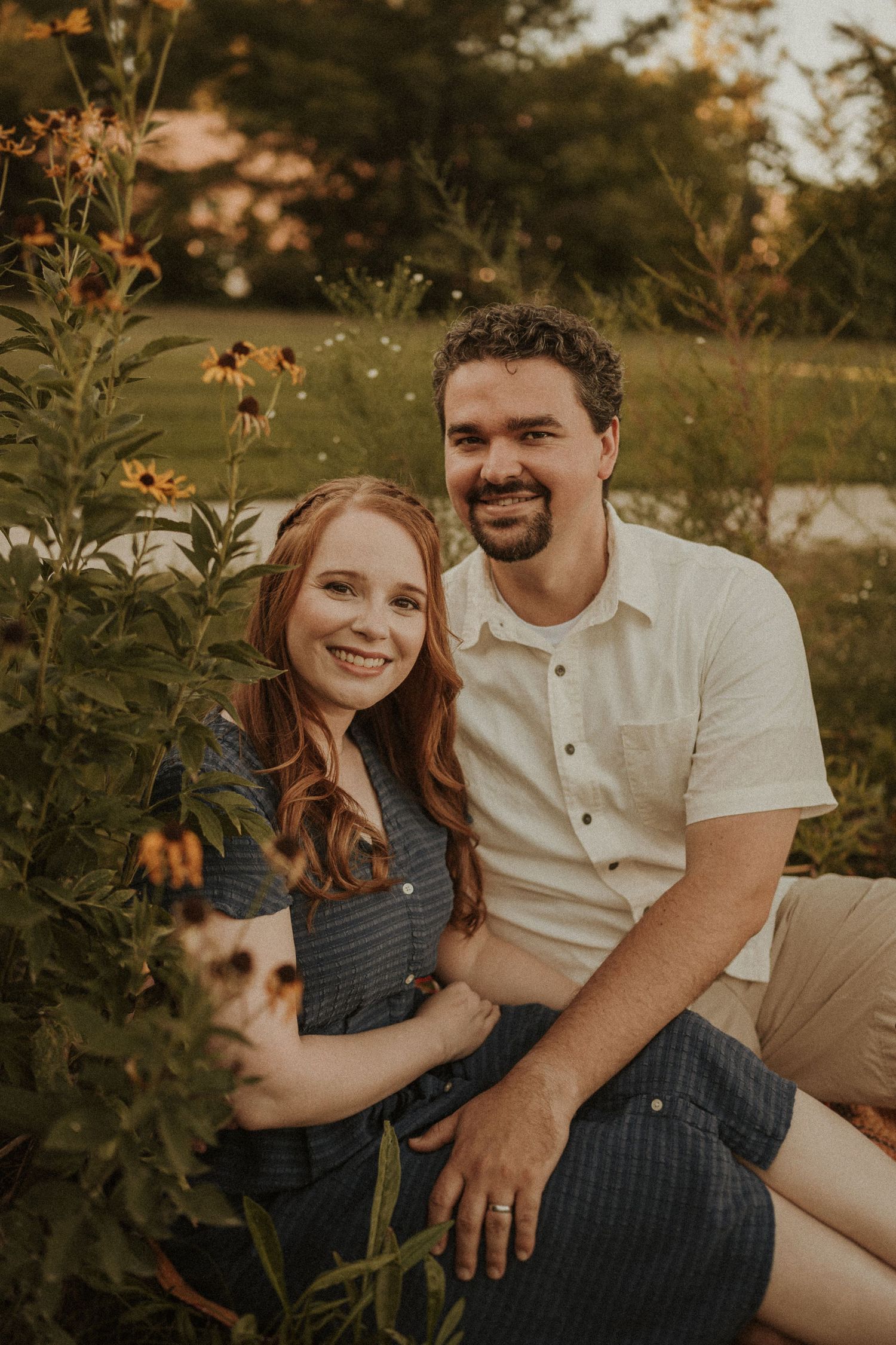 Couple posing together in a garden with blooming wildflowers at sunset.