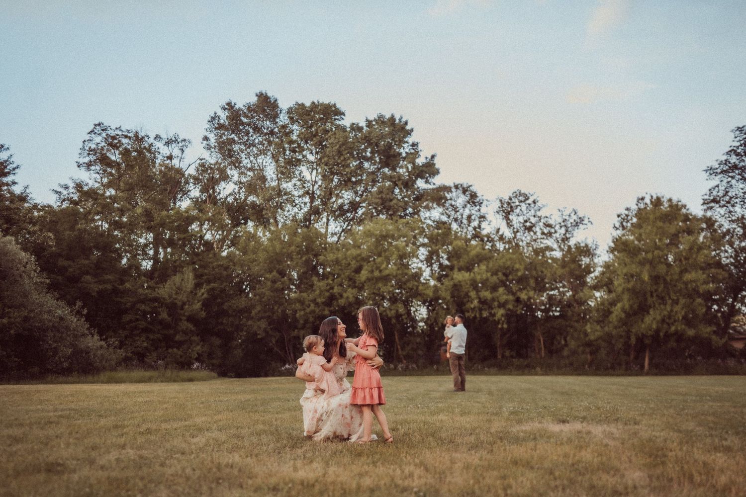 A family enjoying a warm summer evening together in an open field surrounded by trees.