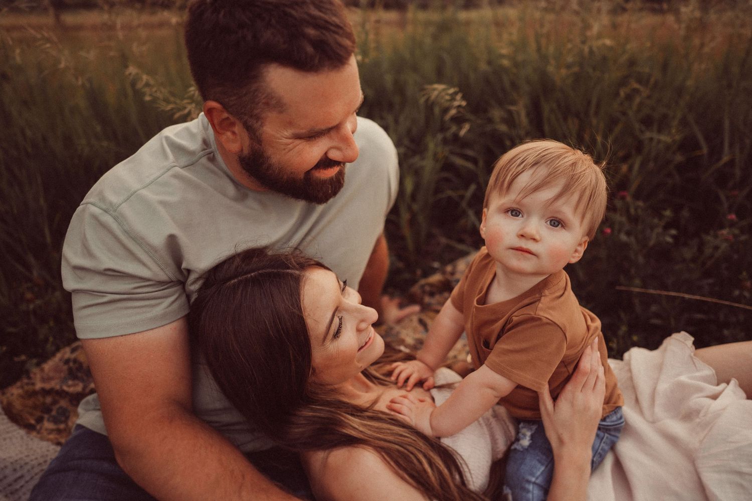 Family sharing a tender moment together while sitting in a grassy field during golden hour.