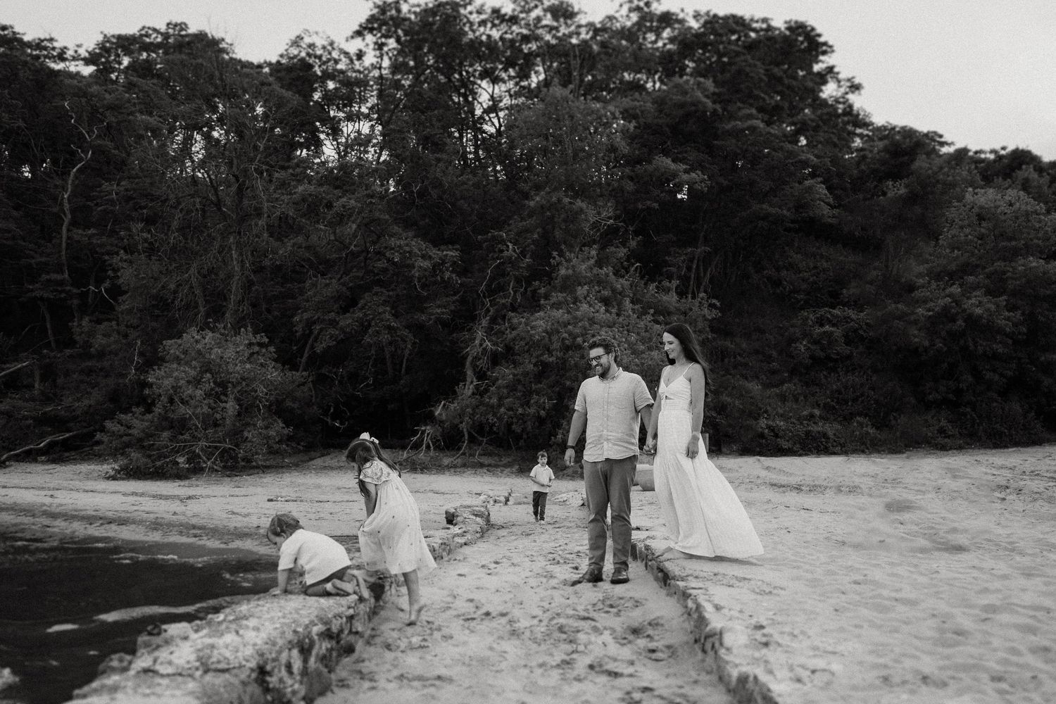 Family group poses together on a beach with trees in background.