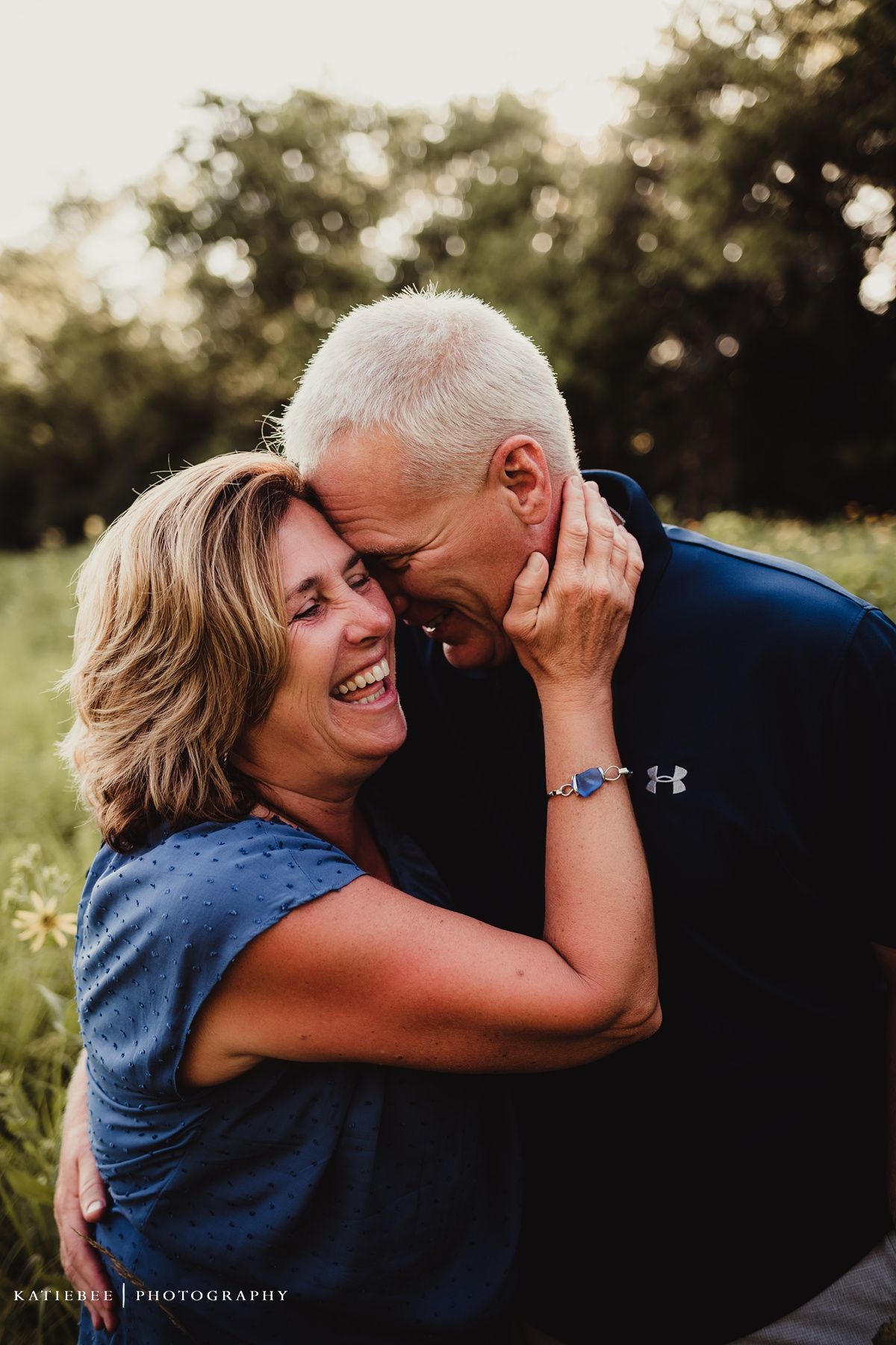 Loving couple shares an intimate moment while laughing together in a sunset meadow.