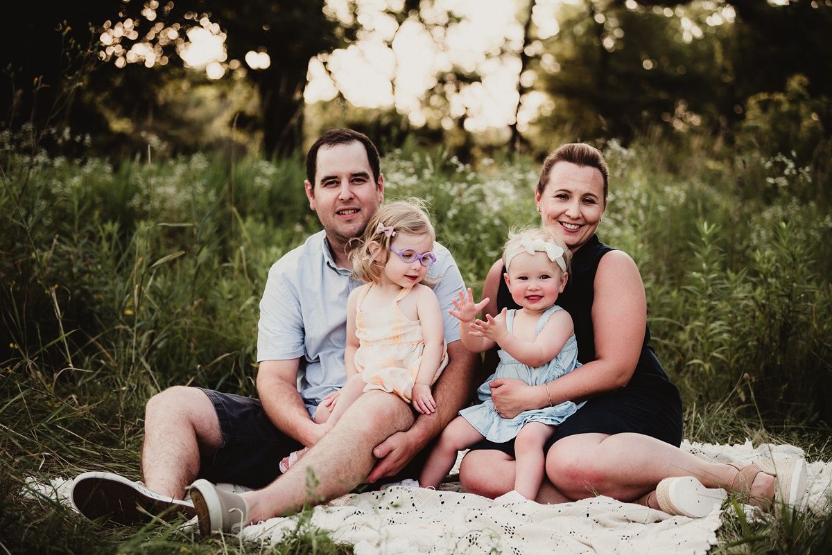 Family relaxing together on a white blanket in a sunlit meadow.