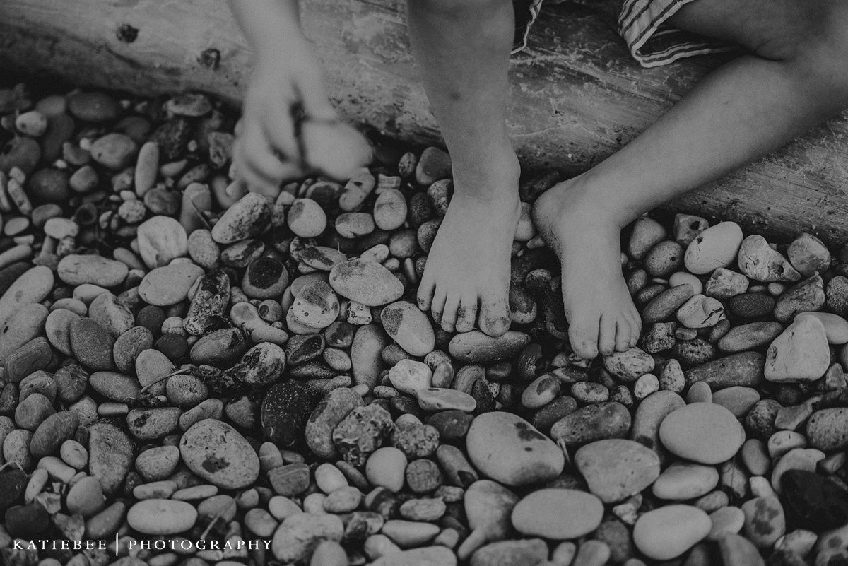 Close-up view of bare feet resting on smooth river rocks by the water.