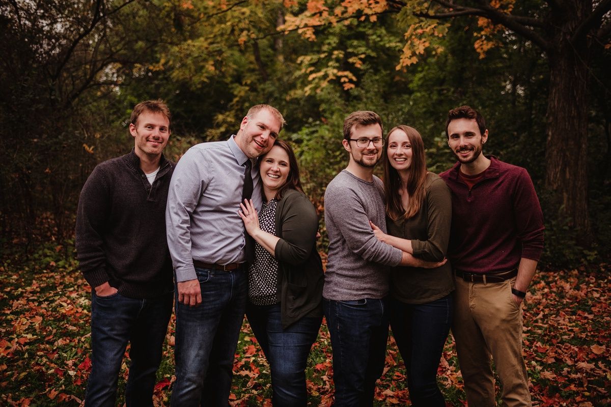 Group of people posing together outdoors with autumn trees and fallen leaves behind them.
