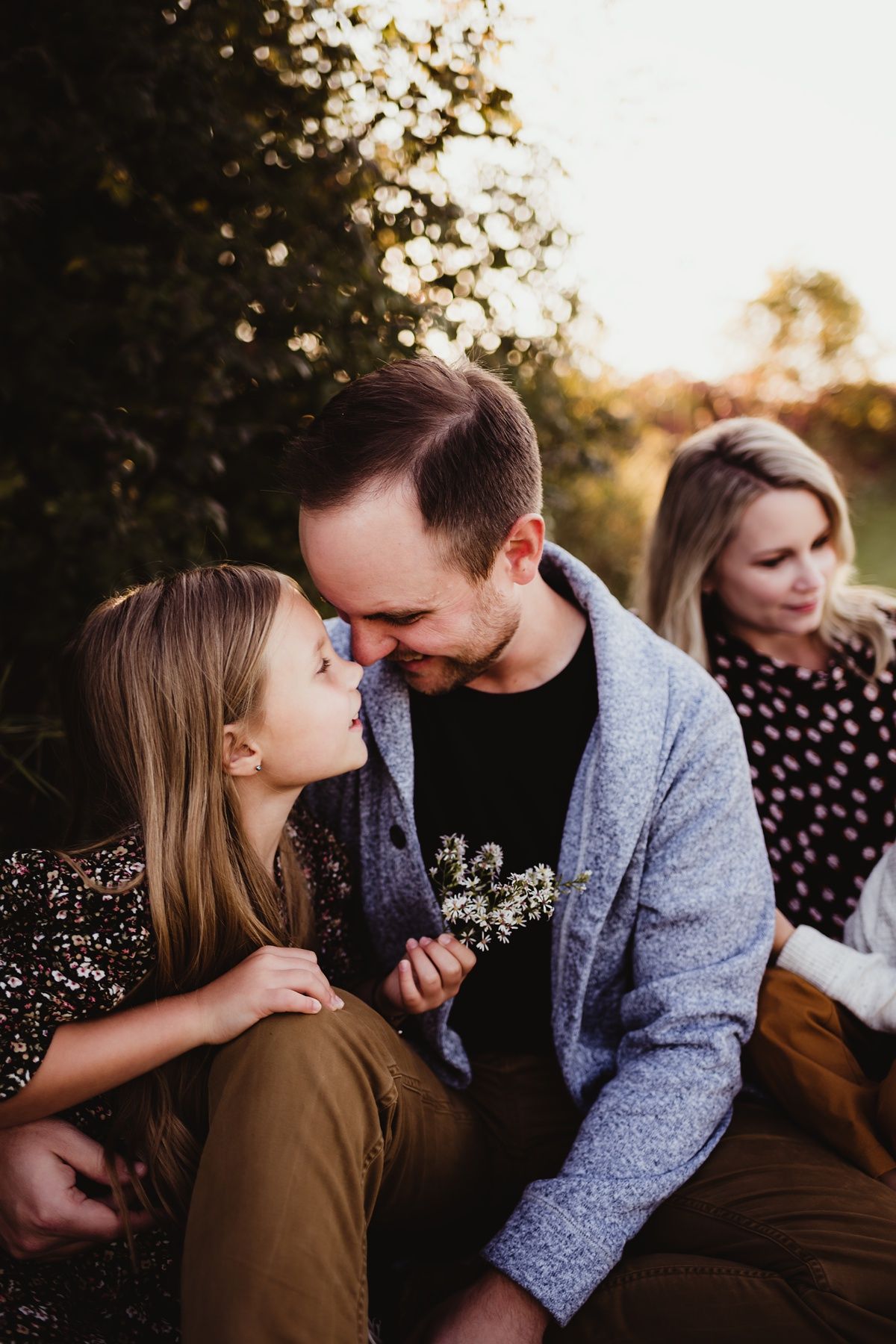 An intimate outdoor family portrait captured during golden hour with bokeh lighting effects.