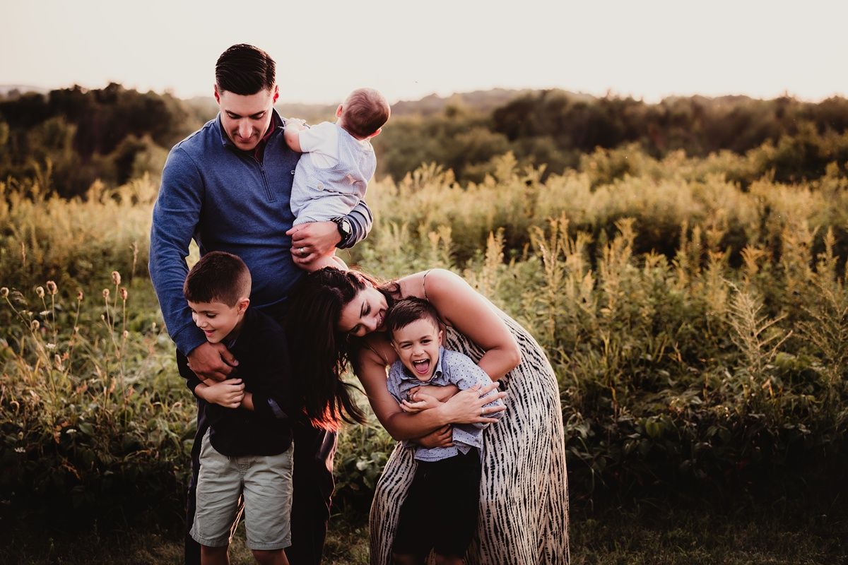 Playful family photo session in a golden field with everyone laughing and being silly.
